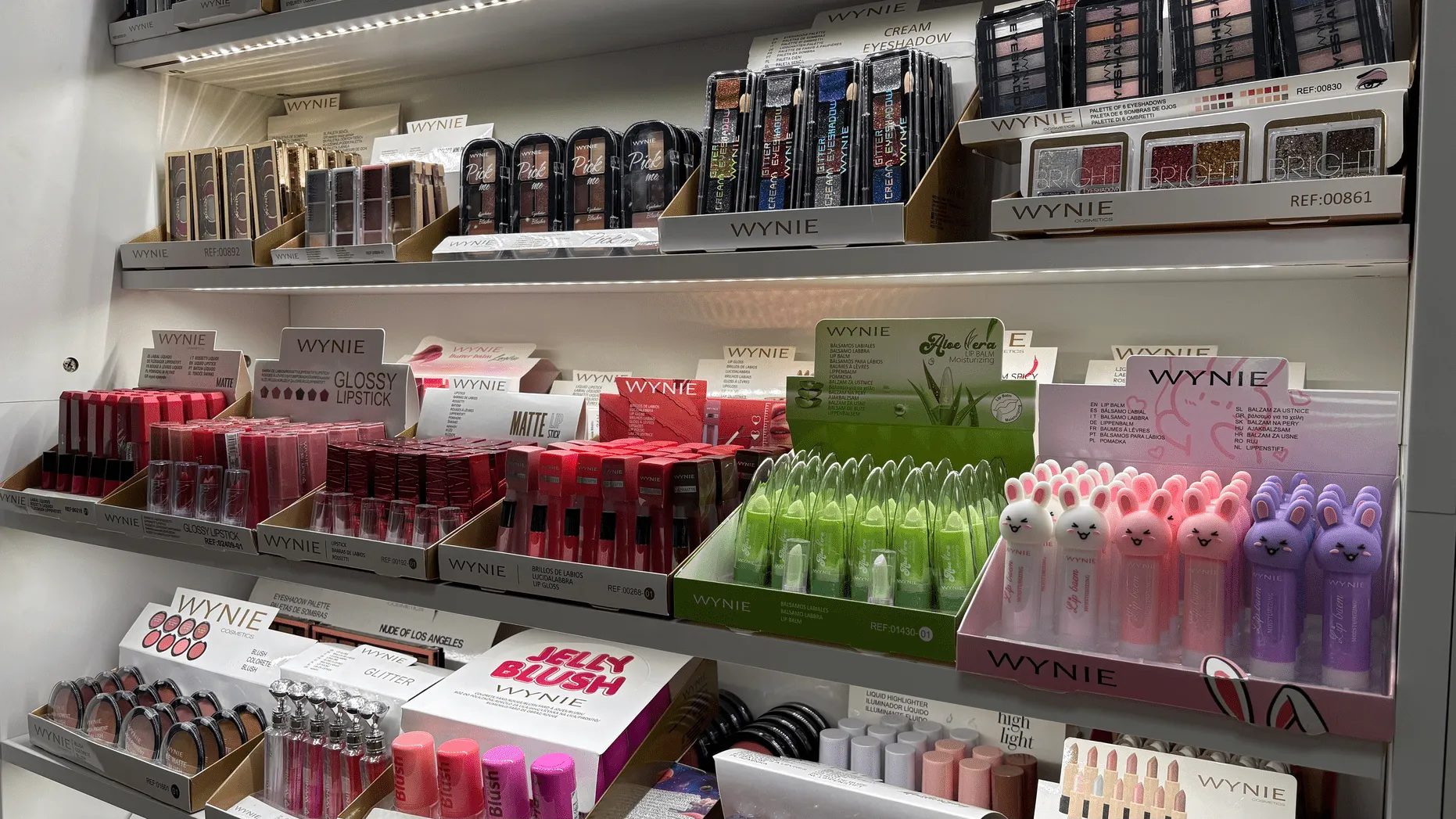 Display shelves with assorted WYNIE makeup products including lipsticks, gloss, lip balm, and eyeshadows.