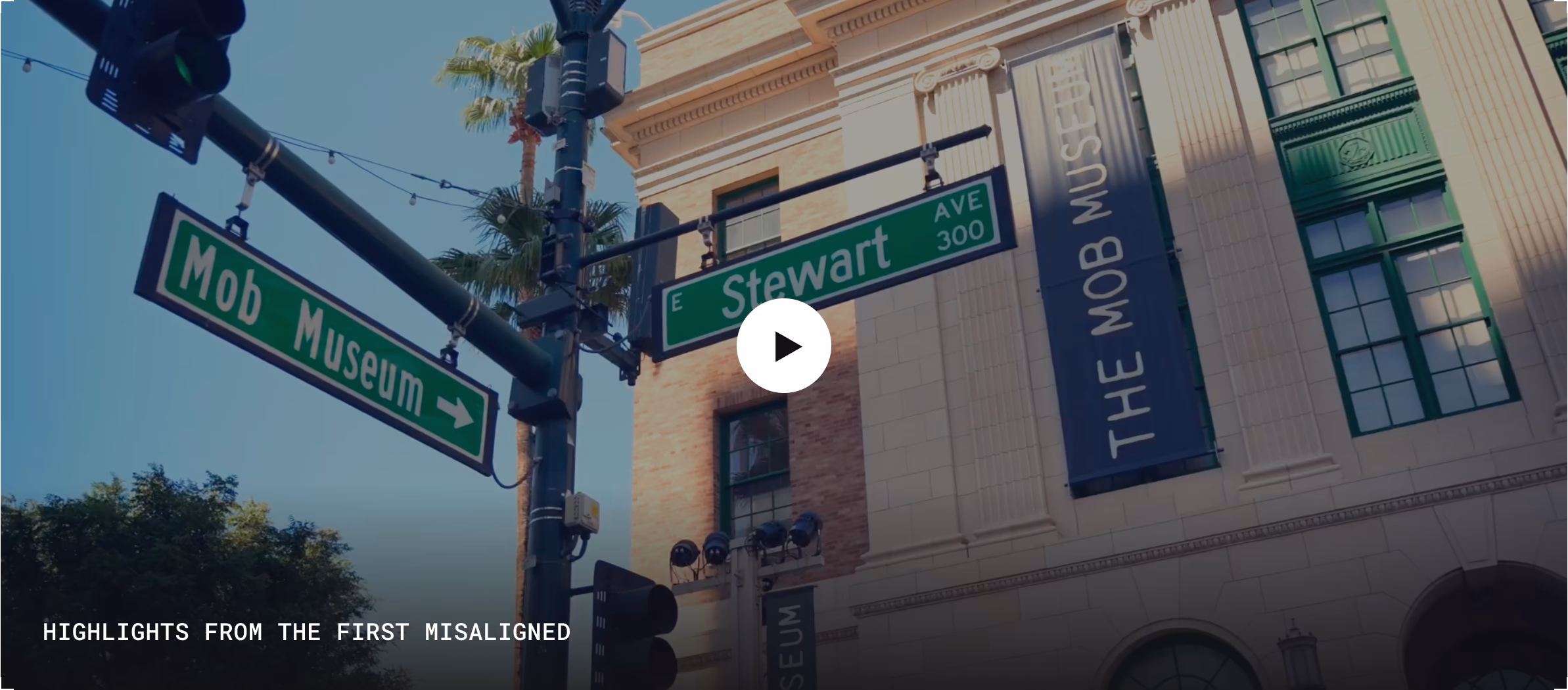 Street signs for Mob Museum and E Stewart Ave on a pole outside a building with Mob Museum banners.