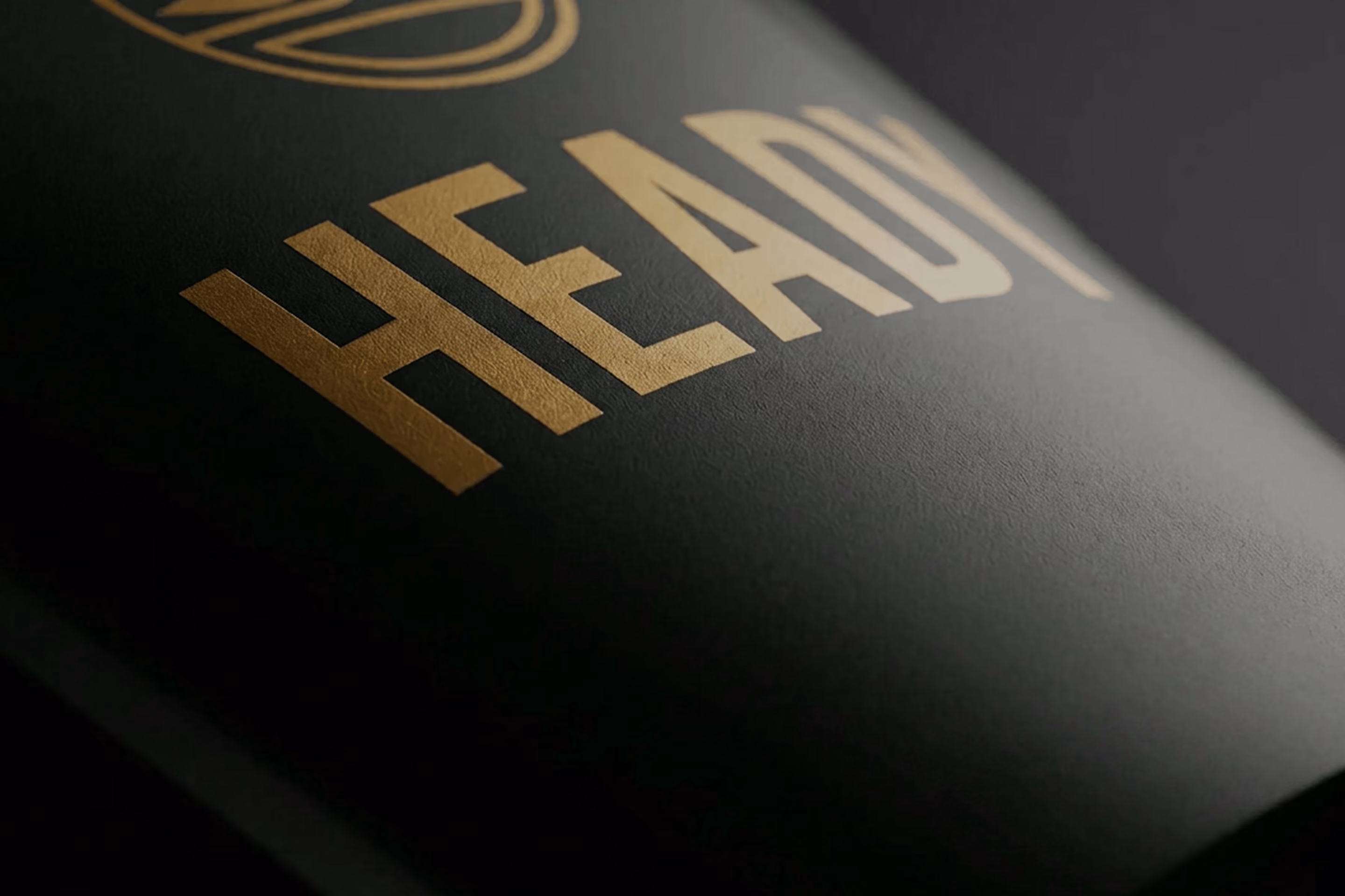 Close-up of gold embossed word 'HEADY' on matte black textured surface.