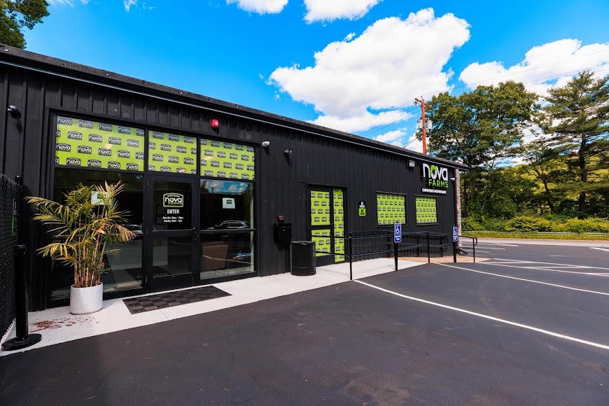 Exterior front view of Nova Farms dispensary, featuring a black building with green-accented window graphics, double glass doors under an "Enter" sign, and an asphalt parking lot in front.