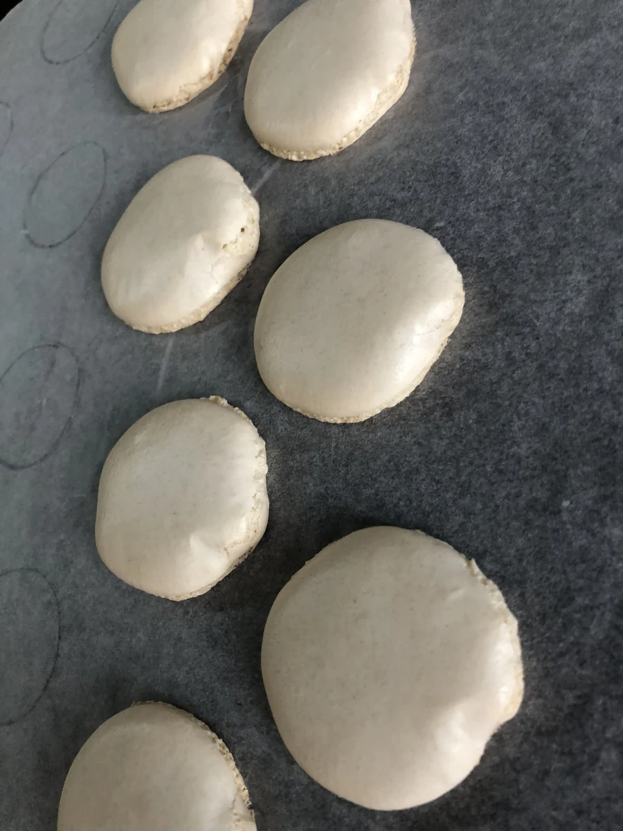 Pale macaron shells with uneven outlines on baking paper