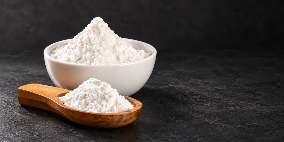 White baking powder in a bowl and wooden scoop