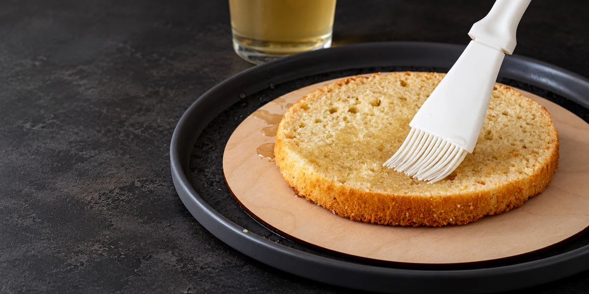 Brushing clear soaking syrup over a sponge cake layer