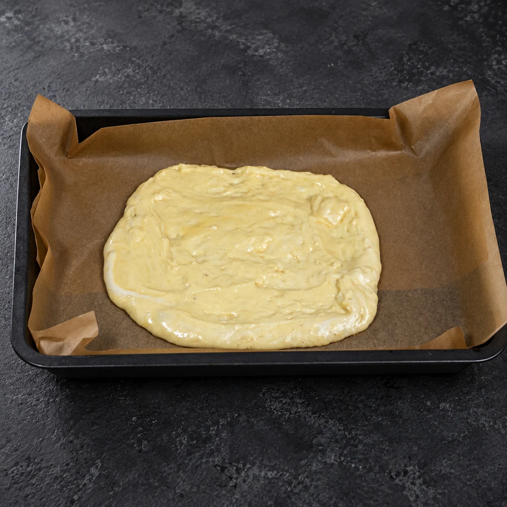 Sponge batter spread on parchment in a baking tray