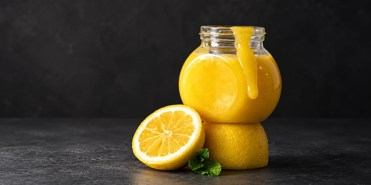 Lemon curd in a glass jar with fresh lemon halves