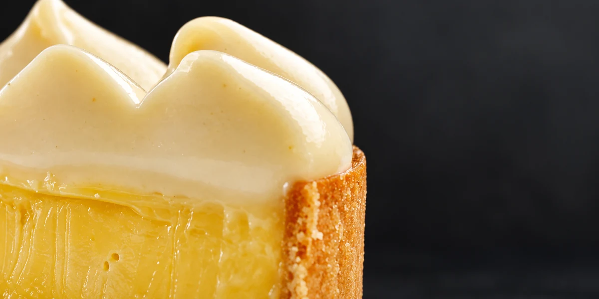 Smooth pale namelaka piped over a tart filling