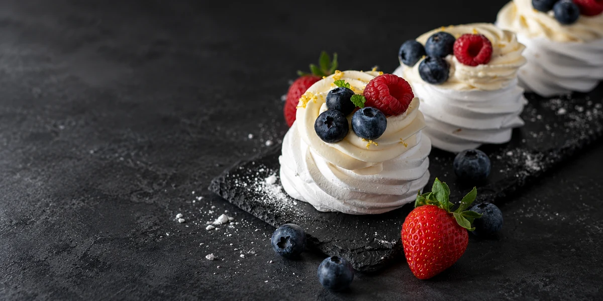 Individual pavlovas topped with cream, strawberries, raspberries and blueberries