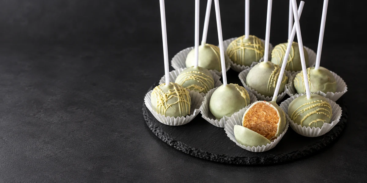 Pale coated cake pops on sticks, with one cut open to show the crumb filling