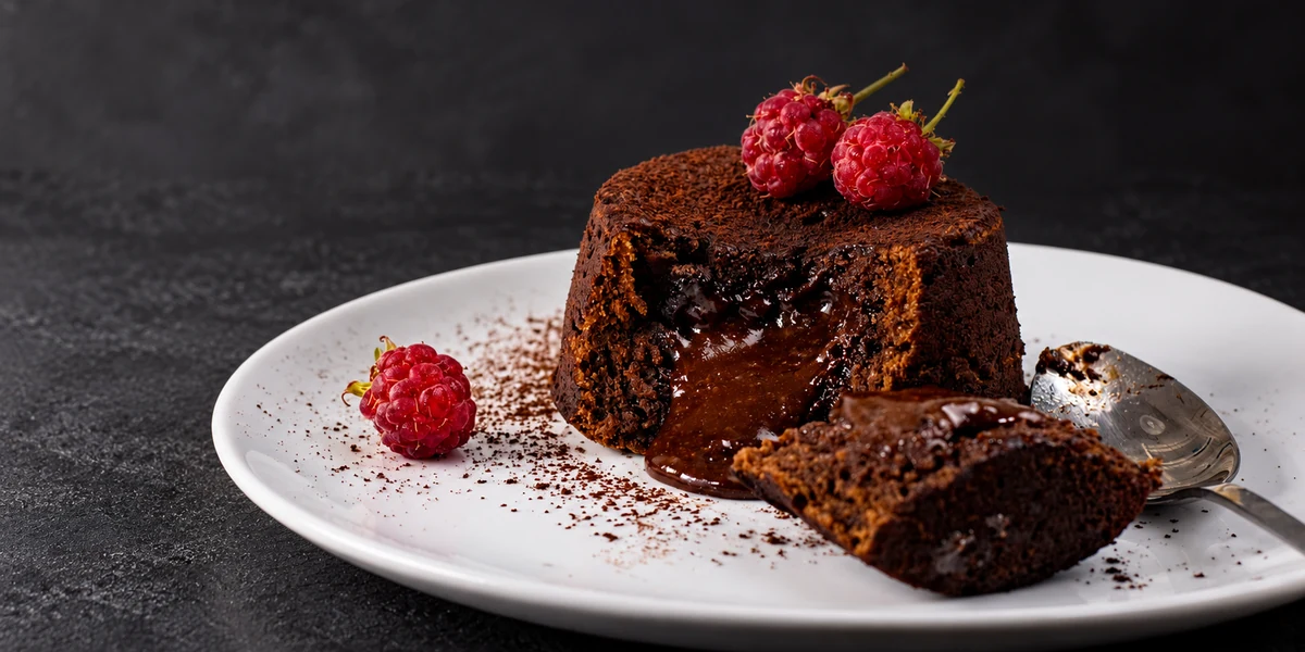 A cut chocolate lava cake with a soft centre and raspberries