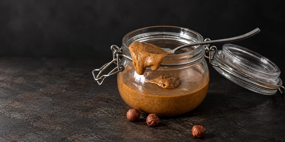 Hazelnut and almond praline paste in a glass jar with a spoon