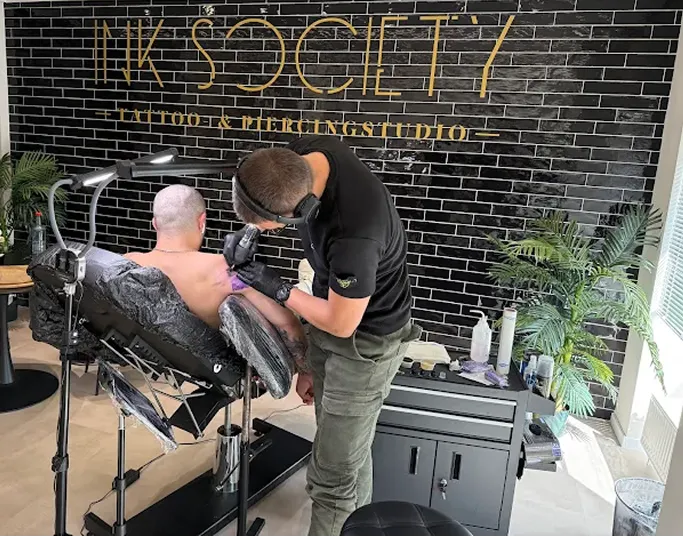 Tätowierer bei der Arbeit im INK SOCIETY Studio Kiel vor Logo-Wand