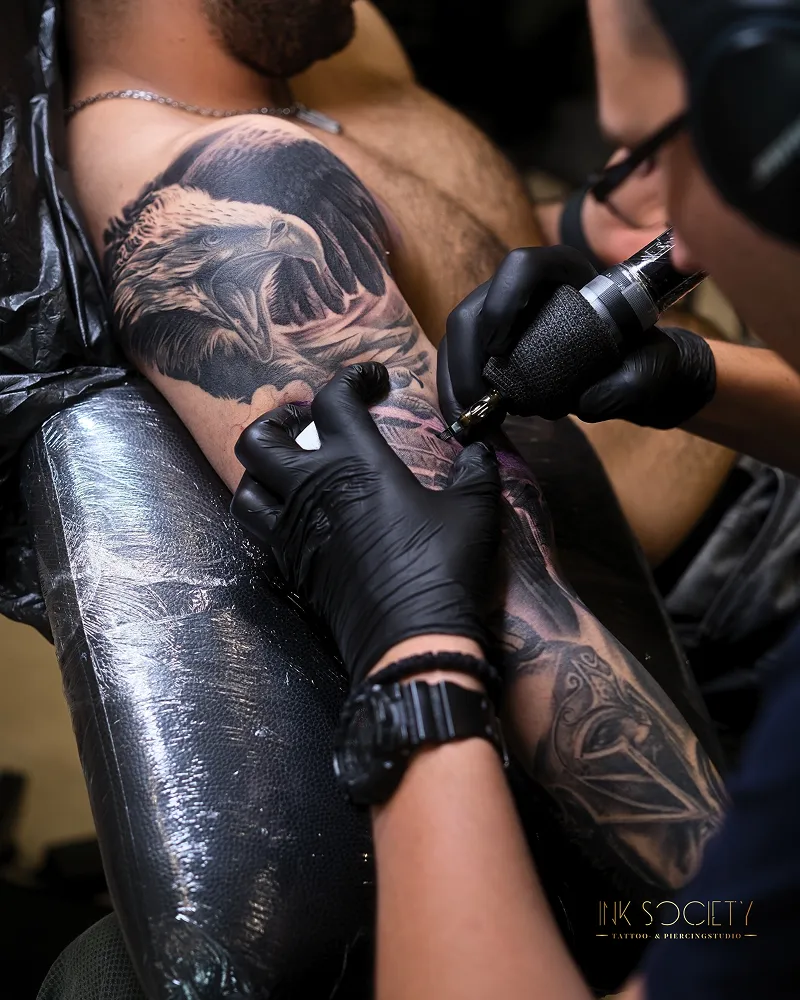Tätowierer mit schwarzen Handschuhen bei der Arbeit an einem Arm-Tattoo