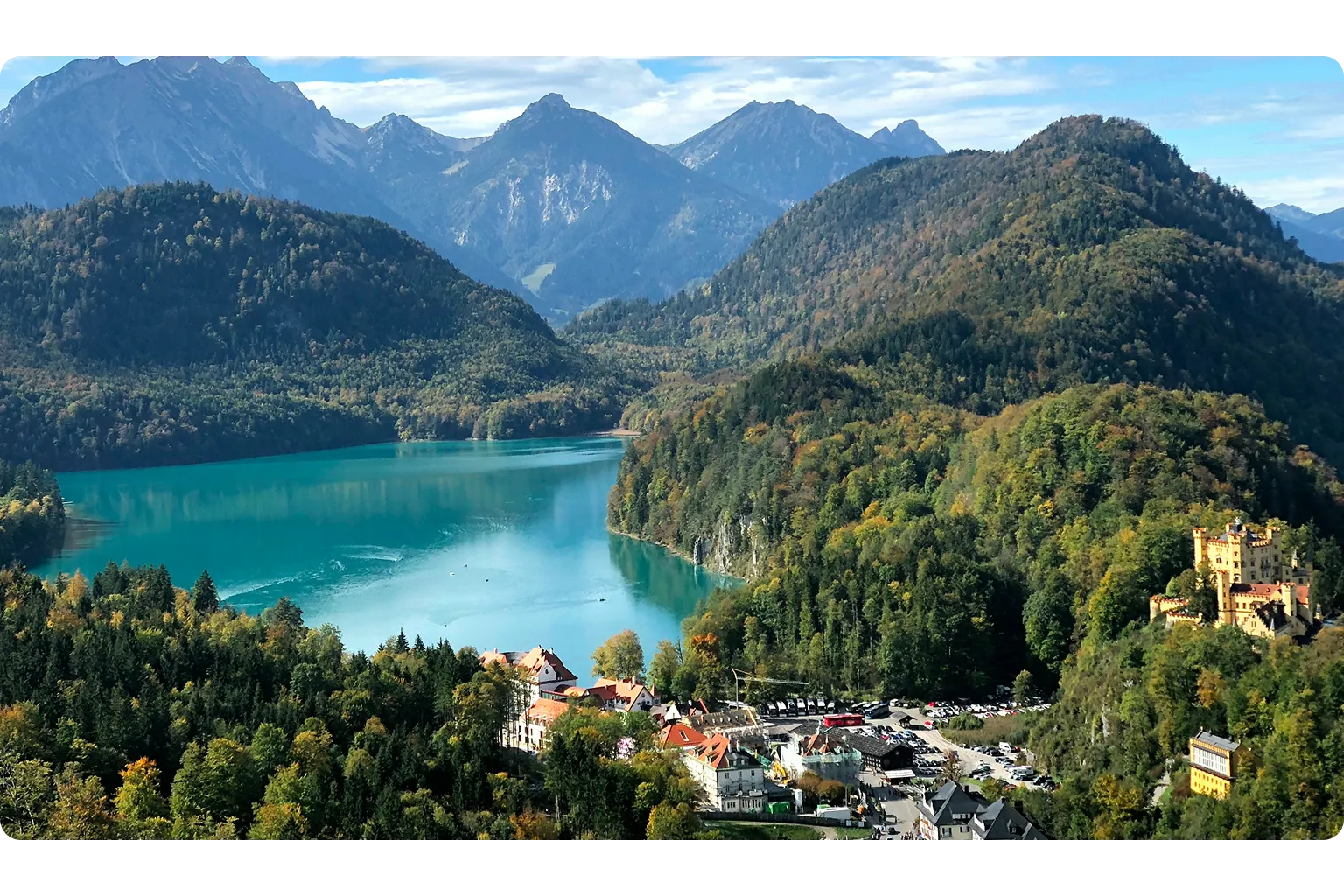 Alpsee in Bayern mit Schloss Hohenschwangau, bewaldeten Bergen und den Bayerischen Alpen im Hintergrund