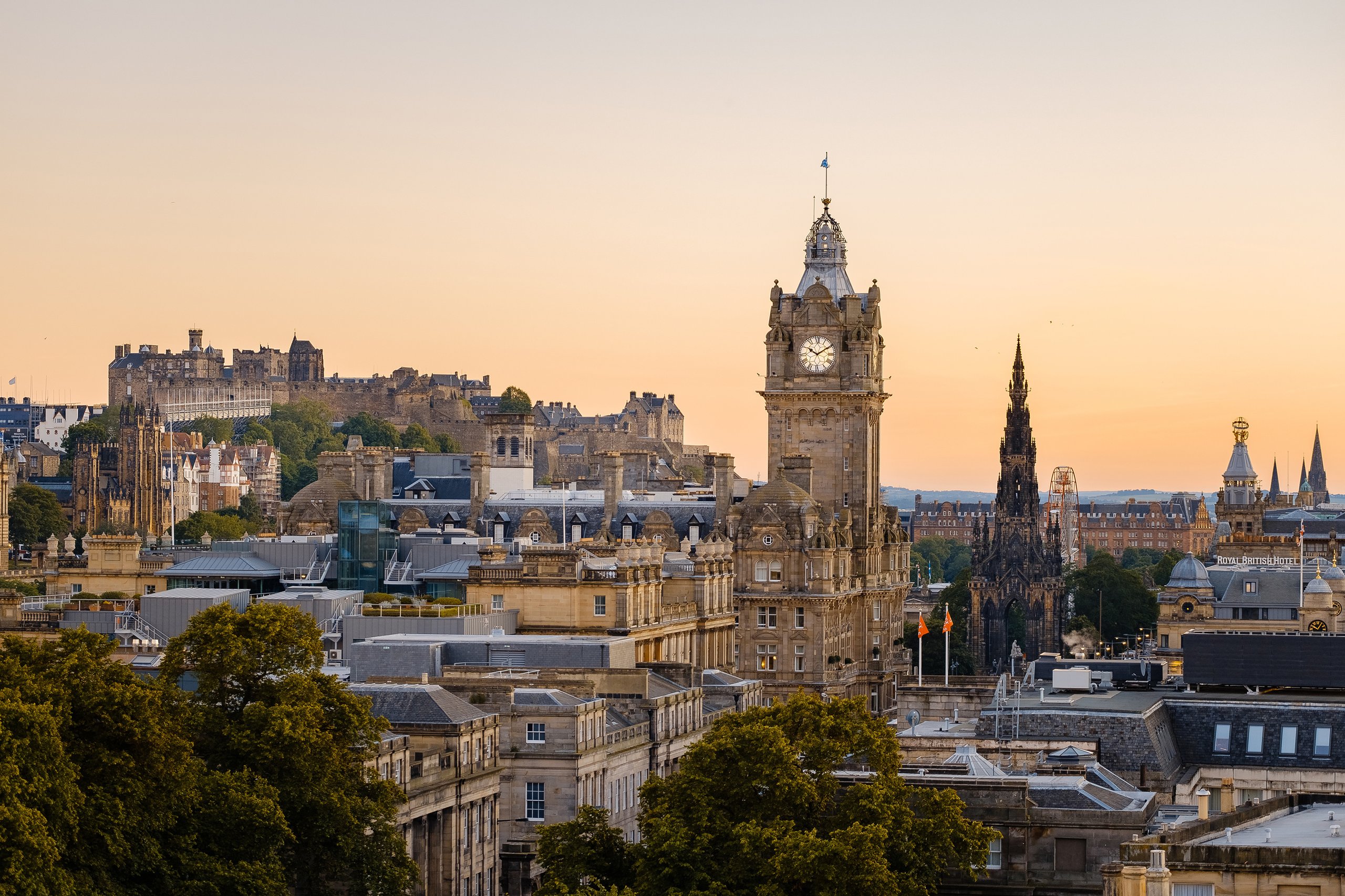 Cityscape of Edinburgh at sunset with Edinburgh Castle and clock tower visible.