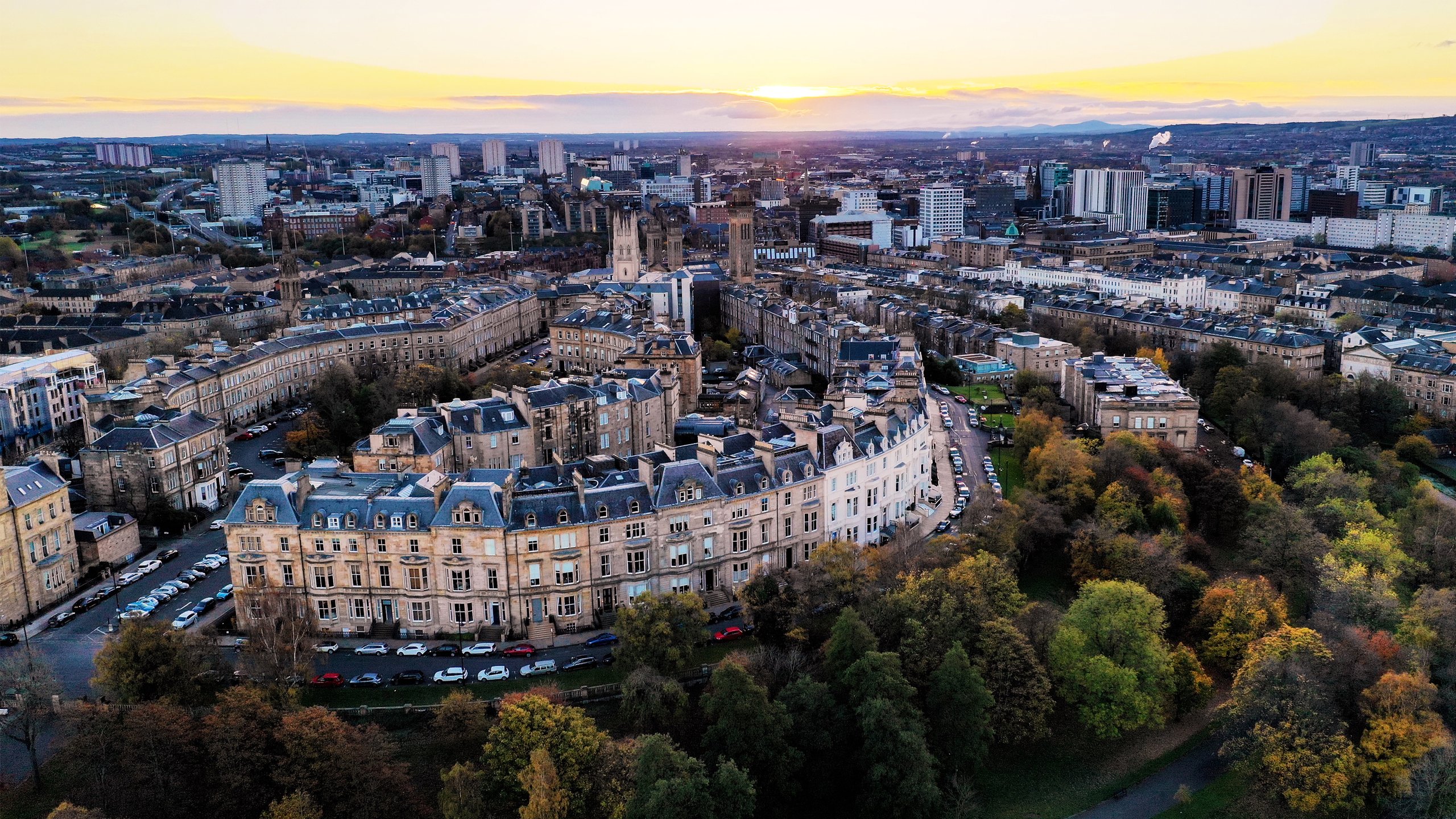 Curved city block with classic buildings surrounded by trees and urban landscape at sunset.