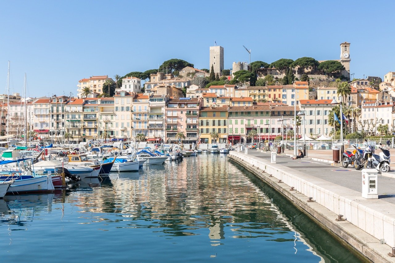 Harbor with moored boats reflecting colorful buildings and historic towers under clear blue sky.