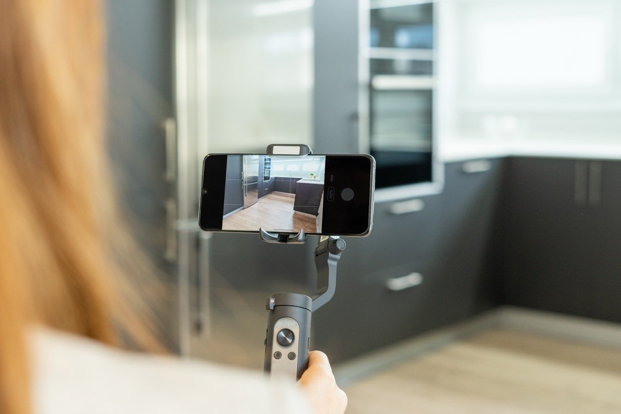 Person filming modern kitchen with smartphone mounted on handheld stabilizer gimbal.
