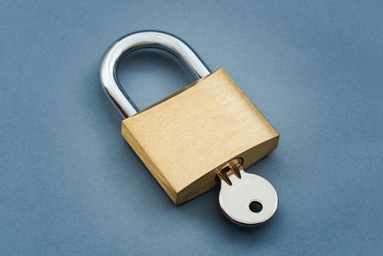 Brass padlock with a silver key partially inserted on a blue background.