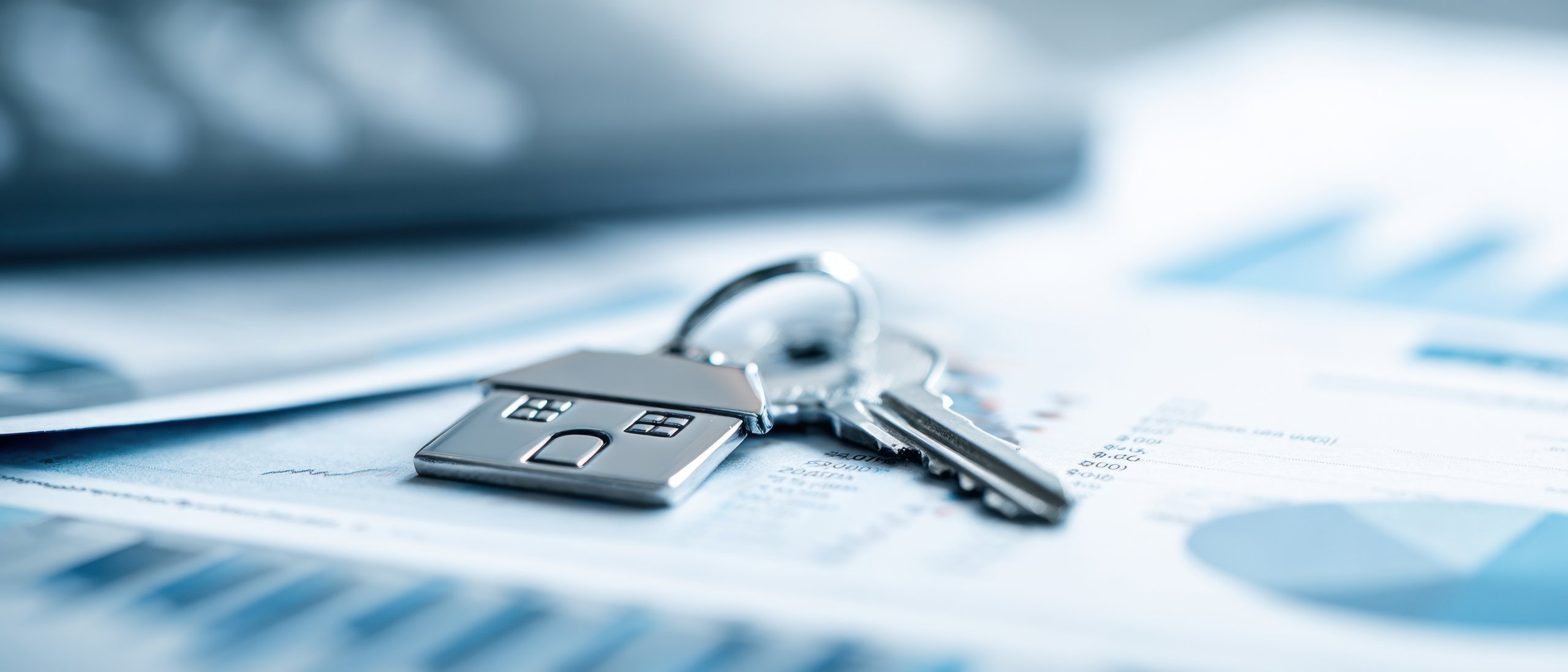 Key with a house-shaped keychain on top of financial documents with charts and graphs.