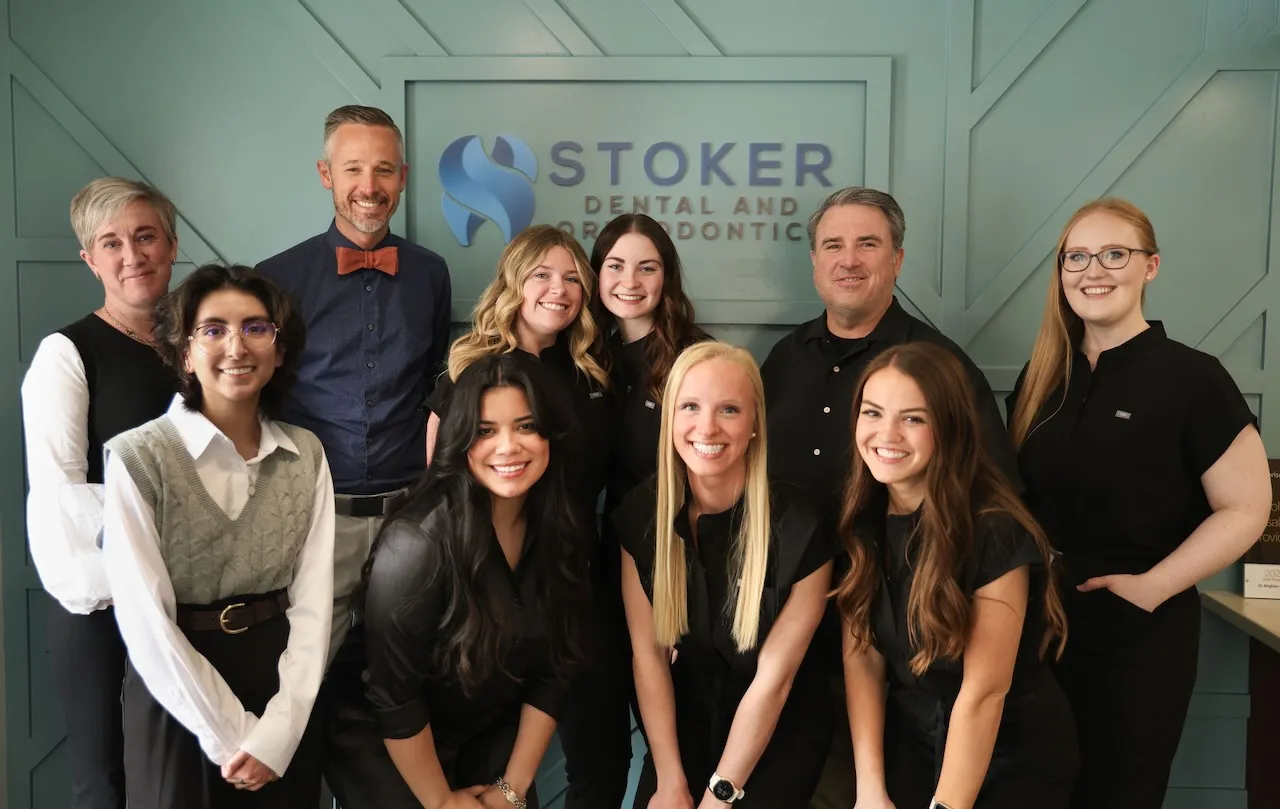 Smiling dental team of six women and two men posing in front of Stoker Dental and Orthodontics sign.
