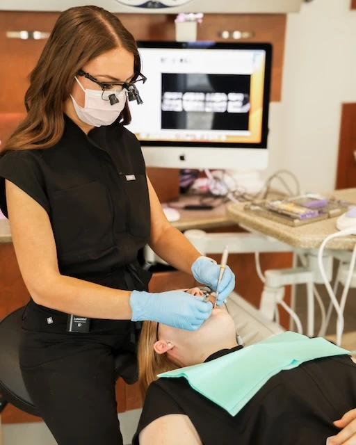 Dentist wearing magnifying glasses and gloves treating a patient lying on the dental chair.