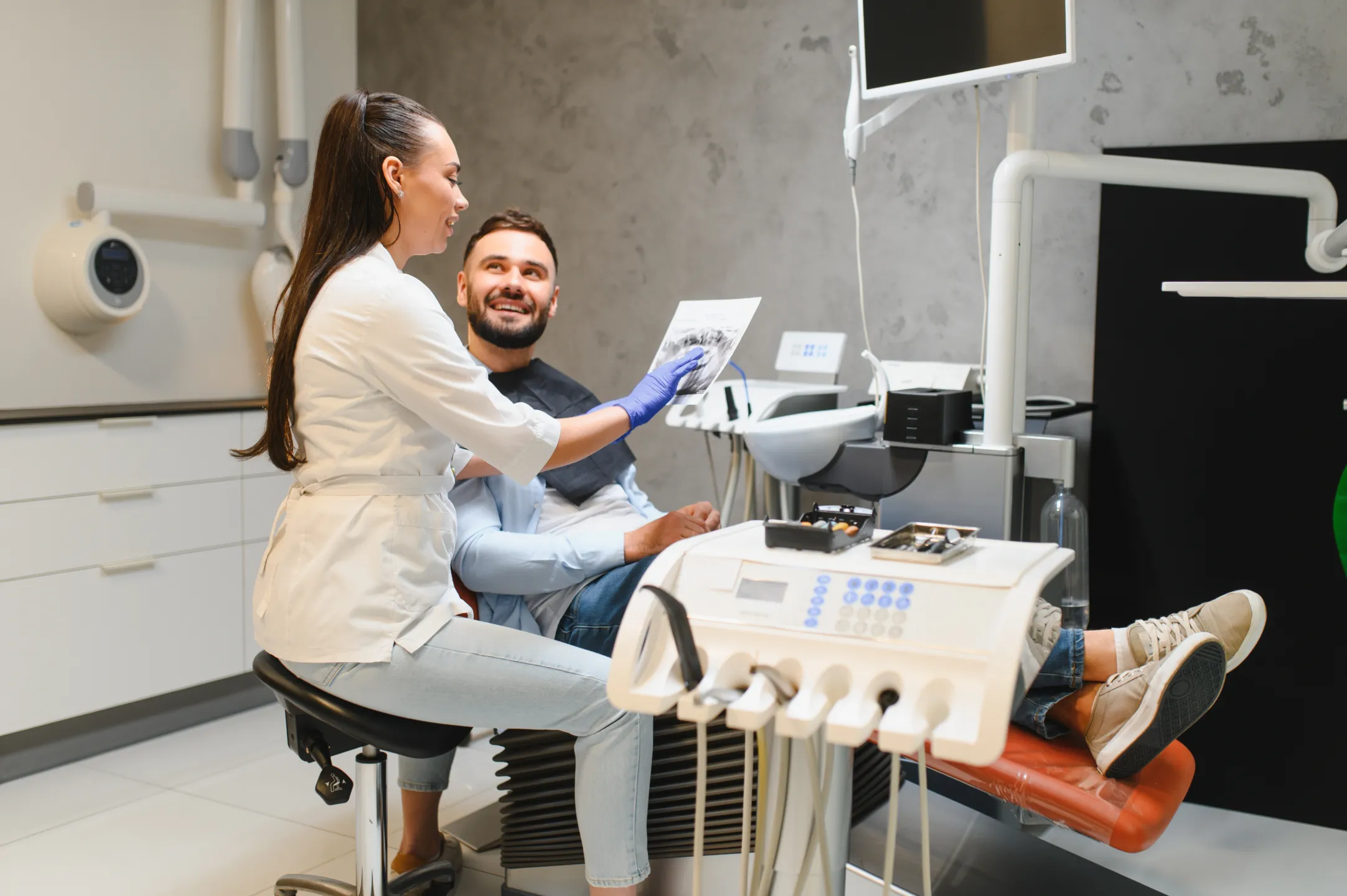 Female dentist showing dental X-ray to a male patient seated in the dental chair.