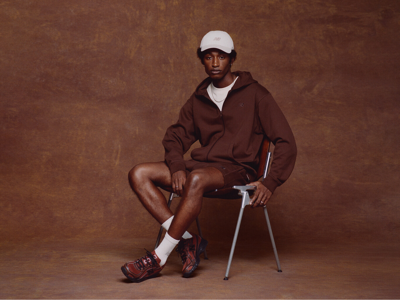 A male model wearing New Balance clothes sitting in the brown background.