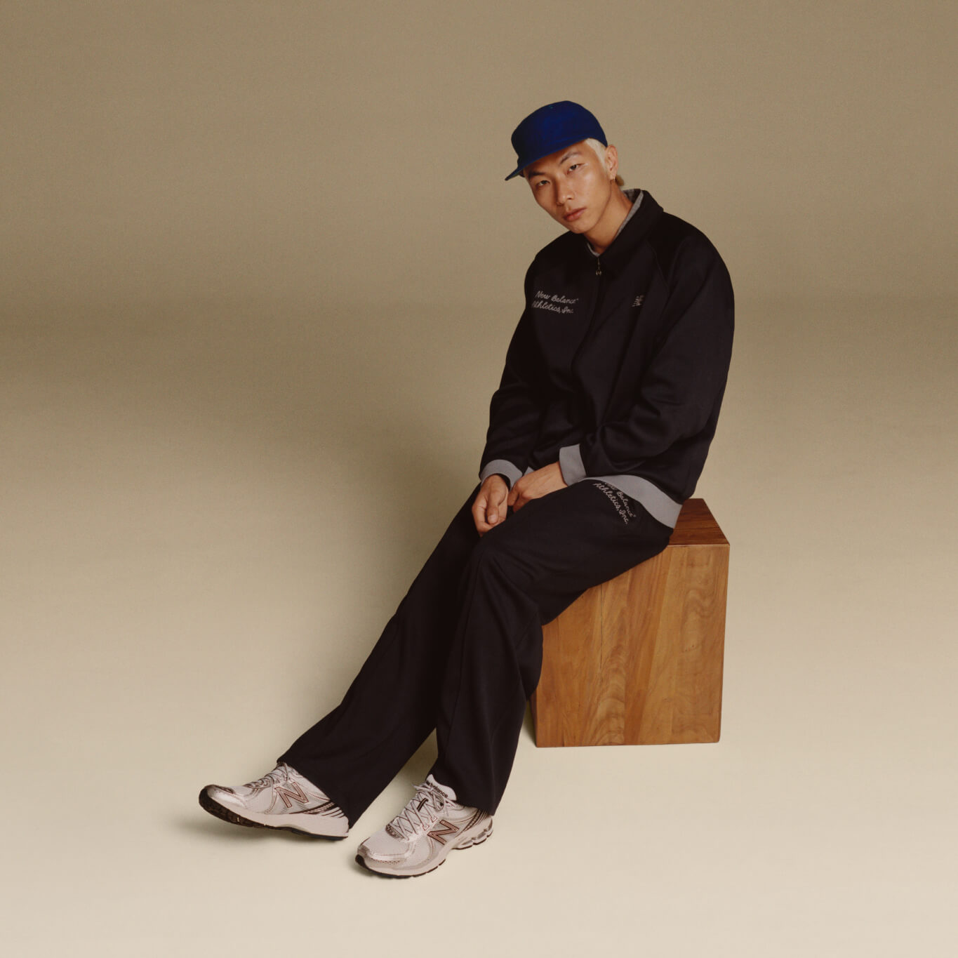 A man wearing New Balance clothes, sitting in light background.