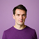 Portrait of a young man with short brown hair wearing a purple shirt against a white background.