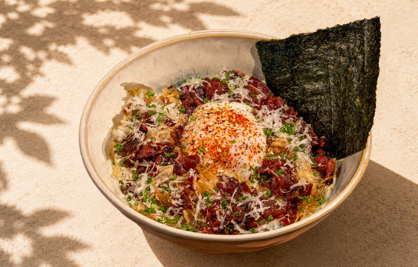 Bowl of rice topped with a seasoned soft-boiled egg, diced meat, herbs, shavings, and seaweed sheets.