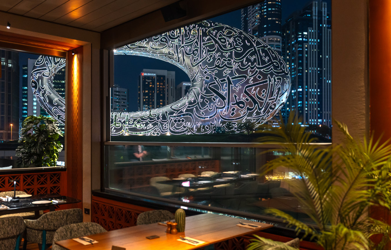Night view of Museum of the Future through restaurant window with tables and plants inside.