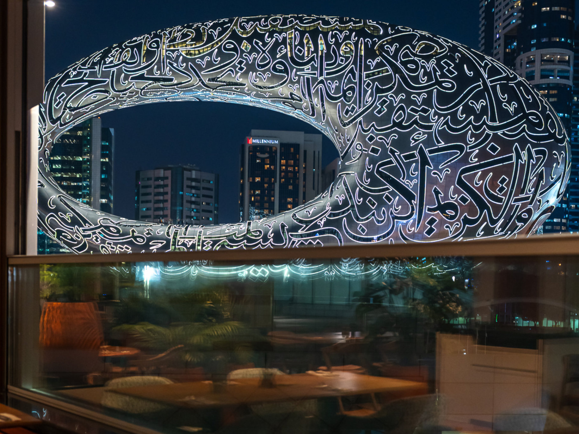 Illuminated Museum of the Future building with Arabic calligraphy in Dubai at night seen through a window.