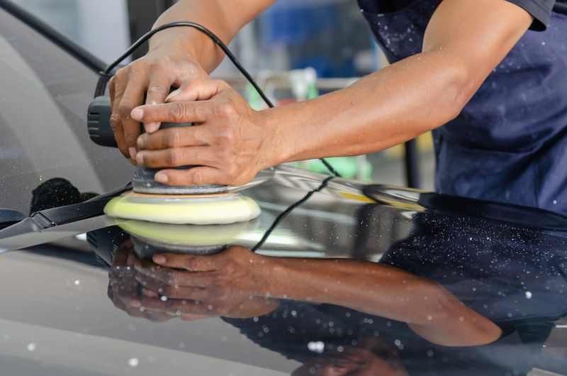 hands buffing a car hood with a polisher