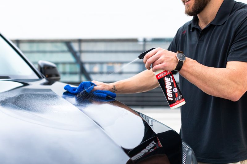 hand applying detail spray and wiping car panel with microfiber cloth
