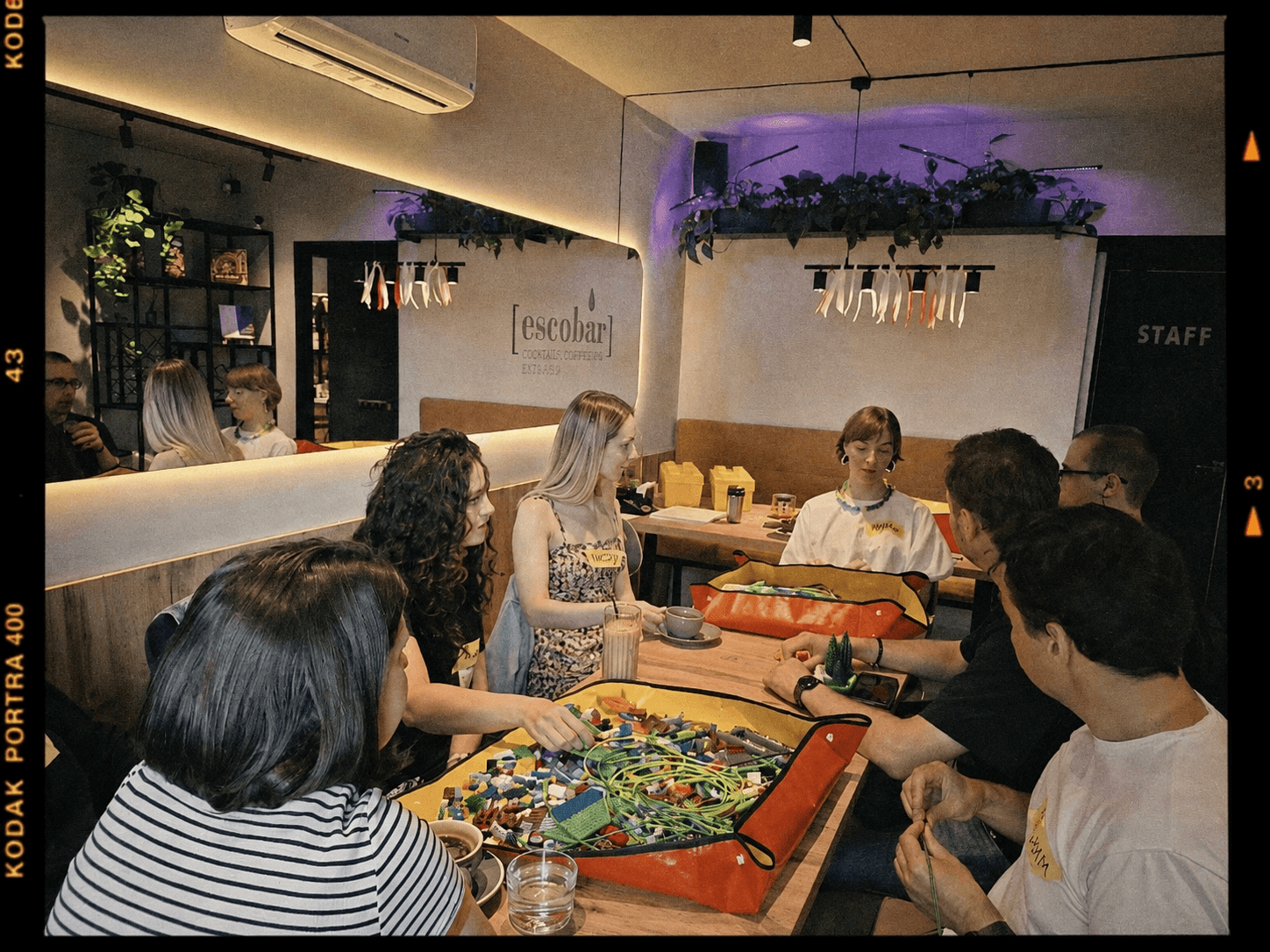 Six people sitting around a table with LEGO pieces and cables in a coffee bar called Escobar.