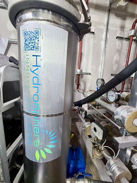 Close-up of a HydroSphere water filtration unit with meters and pipes in a mechanical room.