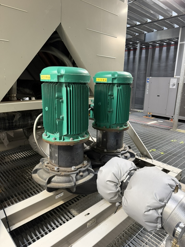 Two green industrial electric motors connected to large black pipes with insulated joints in a metal framework.