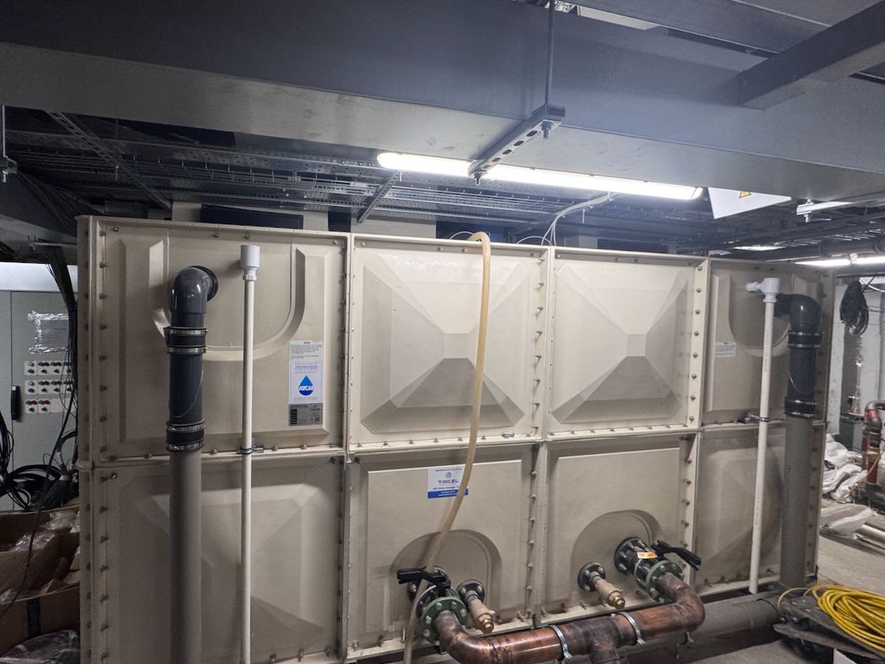 Large industrial water tank with multiple pipes and valves installed in a utility room.