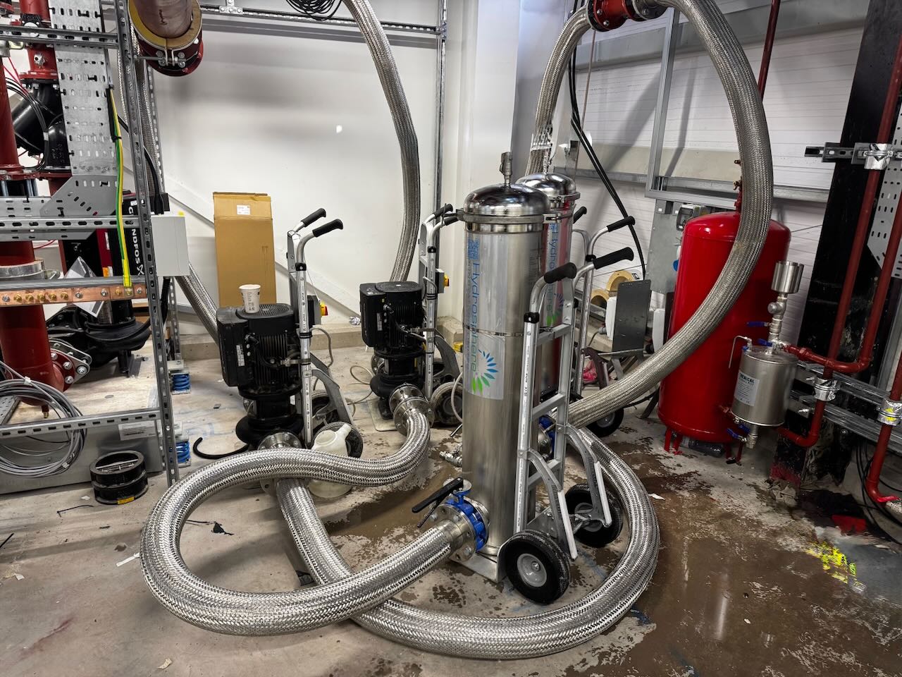 Industrial setup with two stainless steel filtration units on carts connected by thick metal hoses.