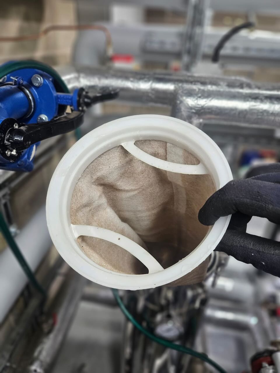 Gloved hand holding open the clean interior of a cylindrical fabric filter in a mechanical room.