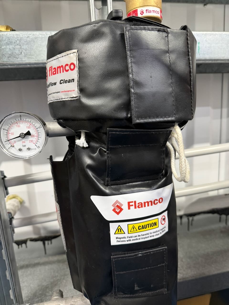 Flamco device with black protective cover and pressure gauge showing psi and bar readings.