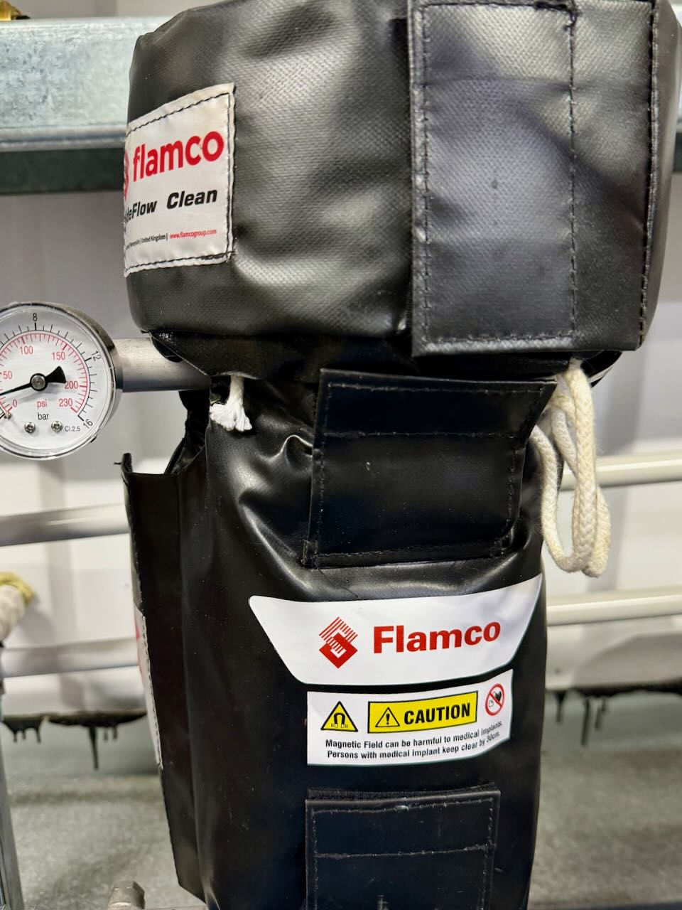 Close-up of Flamco equipment wrapped in black cover with caution label and pressure gauge attached.