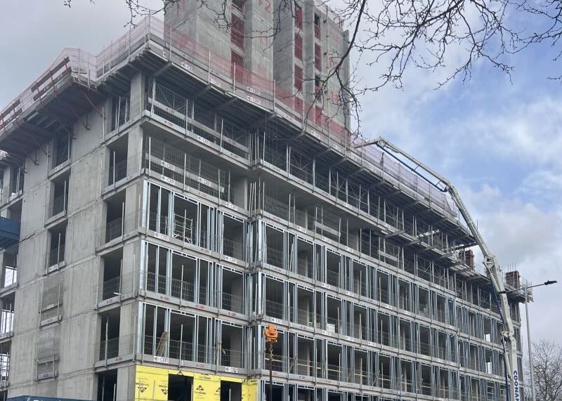 Multi-story concrete building under construction with metal framing and a concrete pump truck.