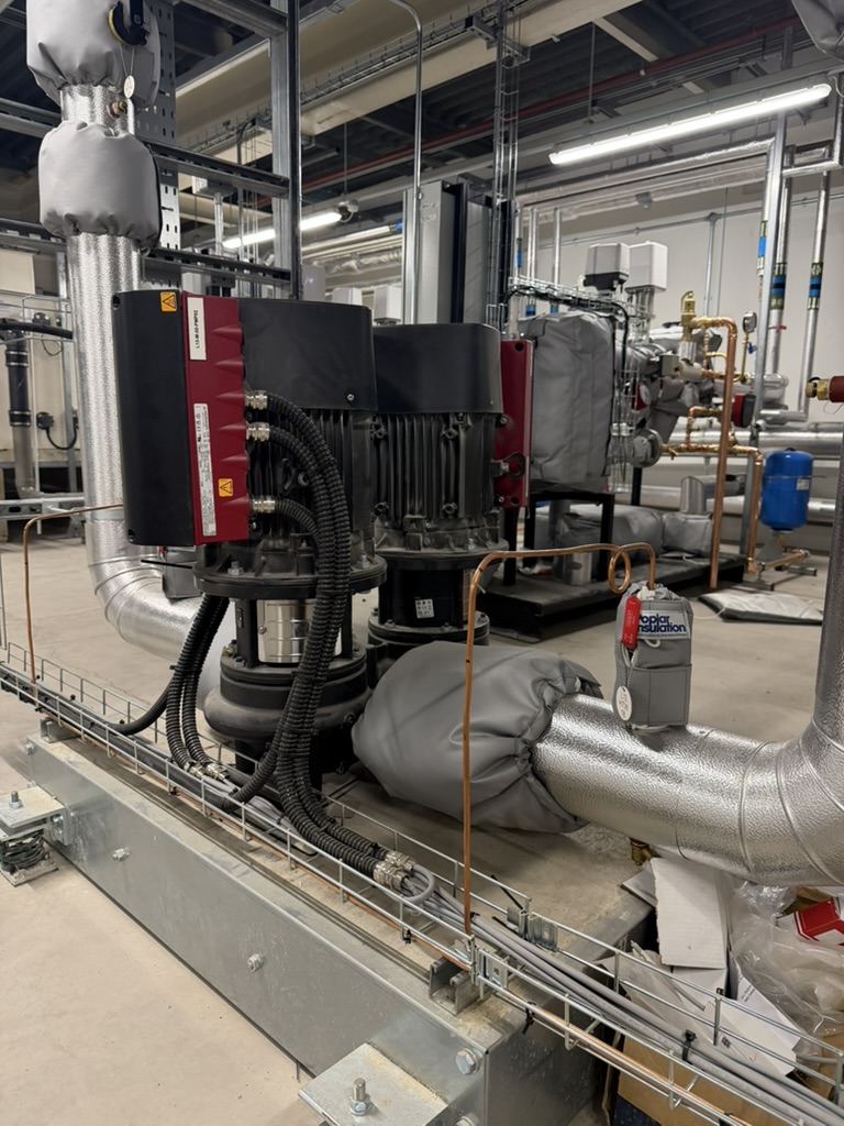 Industrial machinery with insulated pipes, black motors, and connected cables in a factory setting.
