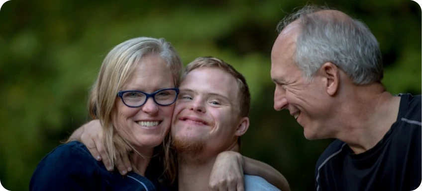 Smiling family embracing outdoors with blurred greenery background.