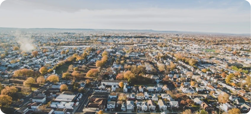 Aerial view of a suburban neighborhood with houses, streets, and trees in autumn colors under a cloudy sky.