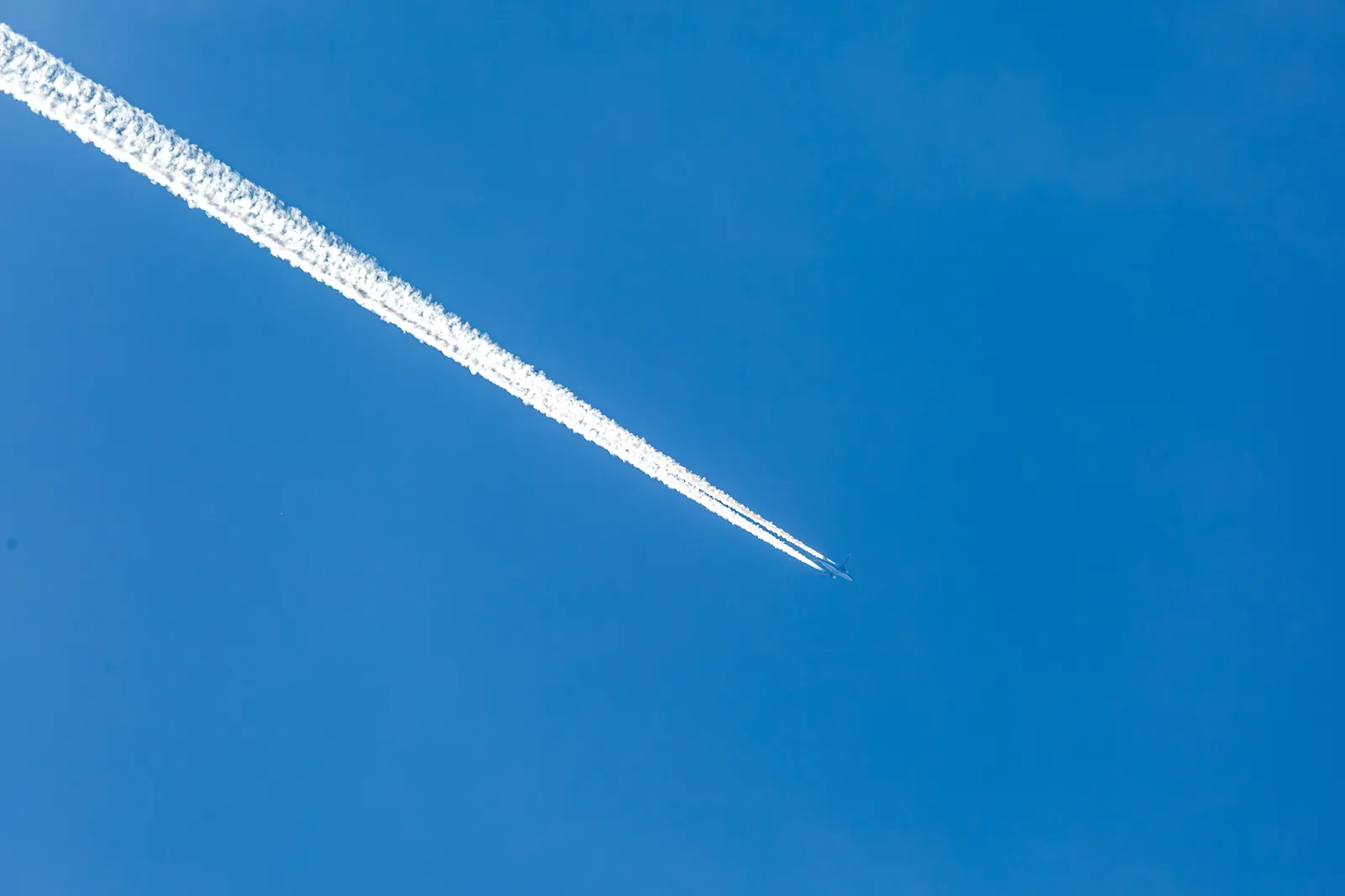 A single high-altitude jet contrail crossing a deep blue sky in the North Atlantic track system