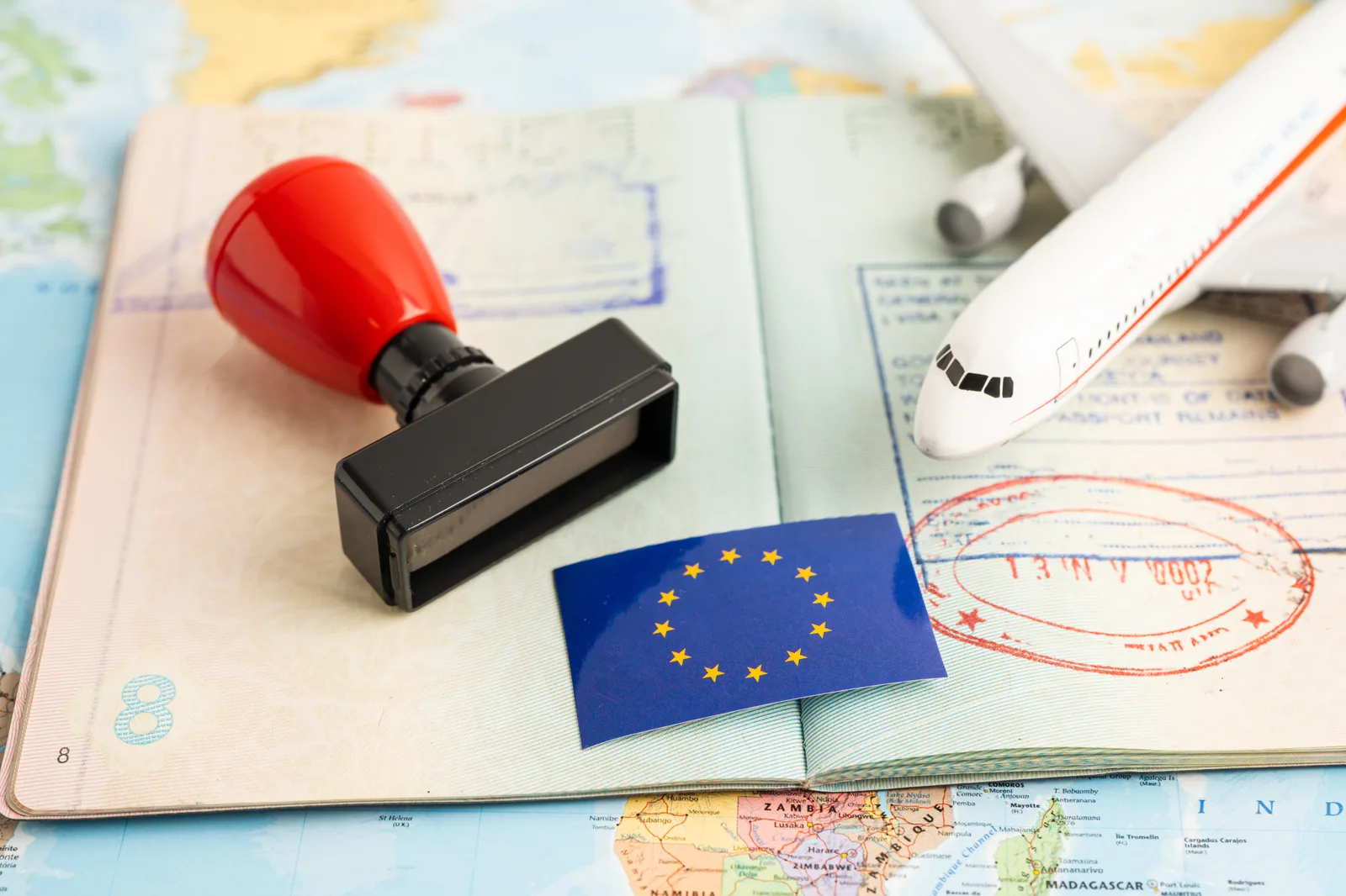 Passport with an entry stamp beside a small model airplane and an EU flag, representing travel into the European Union