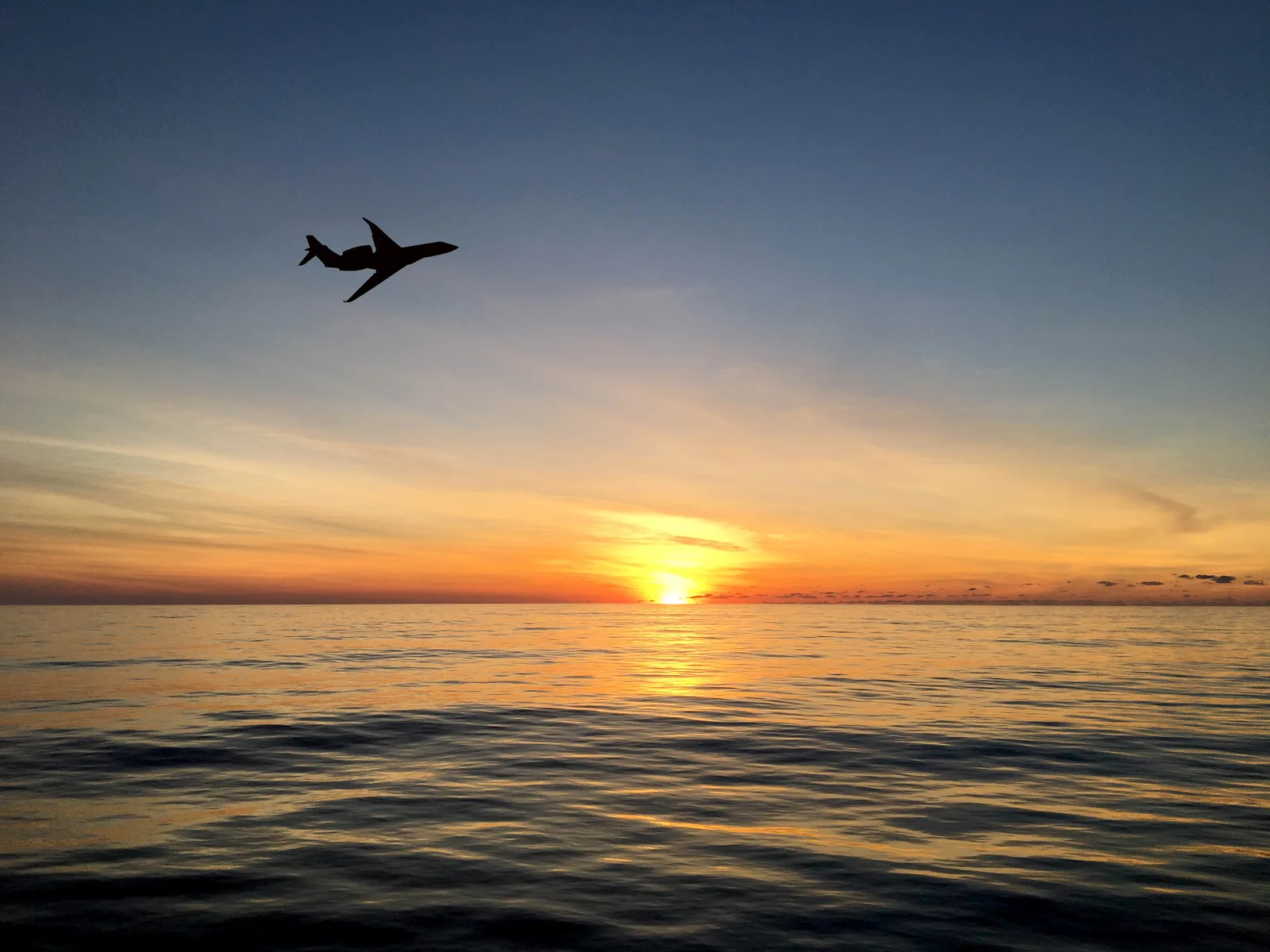 A business jet silhouetted over the open ocean at sunset on an oceanic crossing