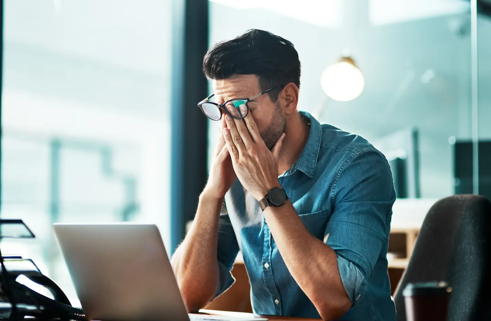 A frustrated professional at a laptop with hands pressed to face